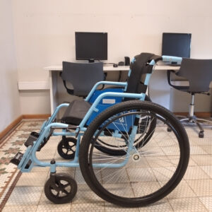 En la foto se representa el prototipo Gen2 XL de una de las sillas de ruedas ubicada en el Servicio de Lectura Accesible. De color negro y celeste. La cual tiene un tamaño apto para todo tipo de cuerpos de personas.
